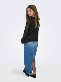 Juoda nėriniuota ilgomis rankovėmis su gėlių raštu, derinama su mėlyna džinsine maxi sijonu su kišenėmis ir šoniniu plyšiu, dėvima su juodais batais.