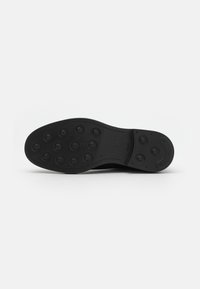 Semelle de chaussure noire avec des motifs de traction circulaires, texture lisse et bords arrondis ; présente un logo et une empreinte de taille sur le talon.