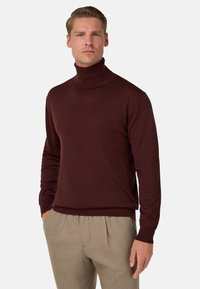 Burgundijas krēmveida turtlenecks džemperis, kas izgatavots no mīksta auduma, ar garām piedurknēm un ribotu apkakli, saskaņots ar gaiši brūnām biksēm.