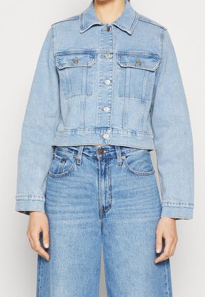 Modèle portant une veste en jean courte délavée claire avec des poches poitrine à boutons et un jean bleu assorti.