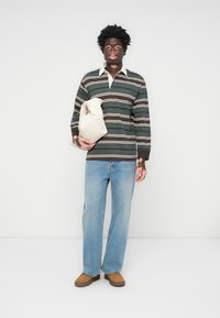 Grønn og hvitstripet langermet skjorte, blå jeans, brune slip-on sko, holder en beige veske. Glatt stoff, avslappet passform, uformell design.