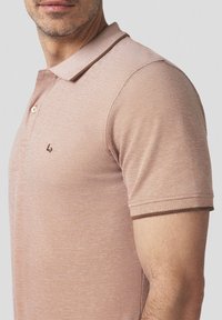 Jasnoróżowa koszulka polo z teksturowanej tkaniny, z małym logo na klatce piersiowej, dwoma guzikami oraz kontrastowym wykończeniem kołnierzyka i rękawów.