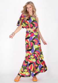 Farverig to-delt outfit bestående af en skuldertop med puffærmer og en lang nederdel med flæsekant, begge i kraftige bladmønstre.