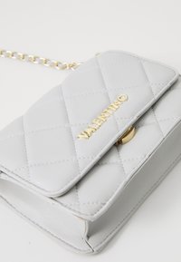 Borsa a tracolla grigia trapuntata in pelle sintetica con logo e hardware dorati, dotata di una tracolla a catena e chiusura a patta.