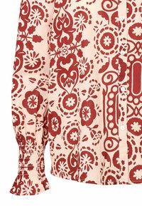 Pitkähihaista nappipaitaa vaalean persikan värisessä kankaassa, jossa on punainen kukkakuosi. Varusteena kootut hihansuut ja klassinen kaulusdesign.