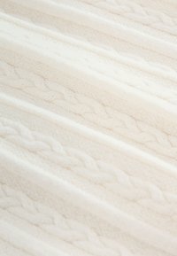 Couverture tricotée blanche avec un motif tressé texturé, alternant des rayures lisses et en relief, montrant douceur et chaleur.