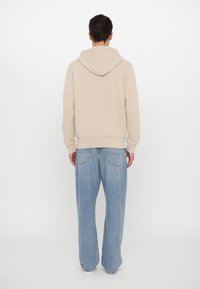 Sudadera con capucha beige de corte relajado, con puños y dobladillo acanalados, combinada con jeans de pierna ancha en azul claro.