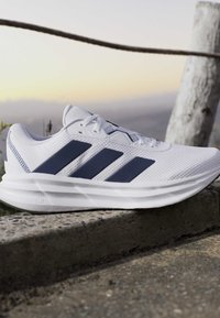 White athletic shoe with black stripes resting on a concrete surface outdoors at sunset.