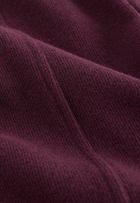 Burgundin kangas, jossa on teksturoitu, uritettu pinta. Materiaali näyttää pehmeältä, ja siinä on näkyviä kuituja sekä hienovaraisia lineaarisia kuvioita.