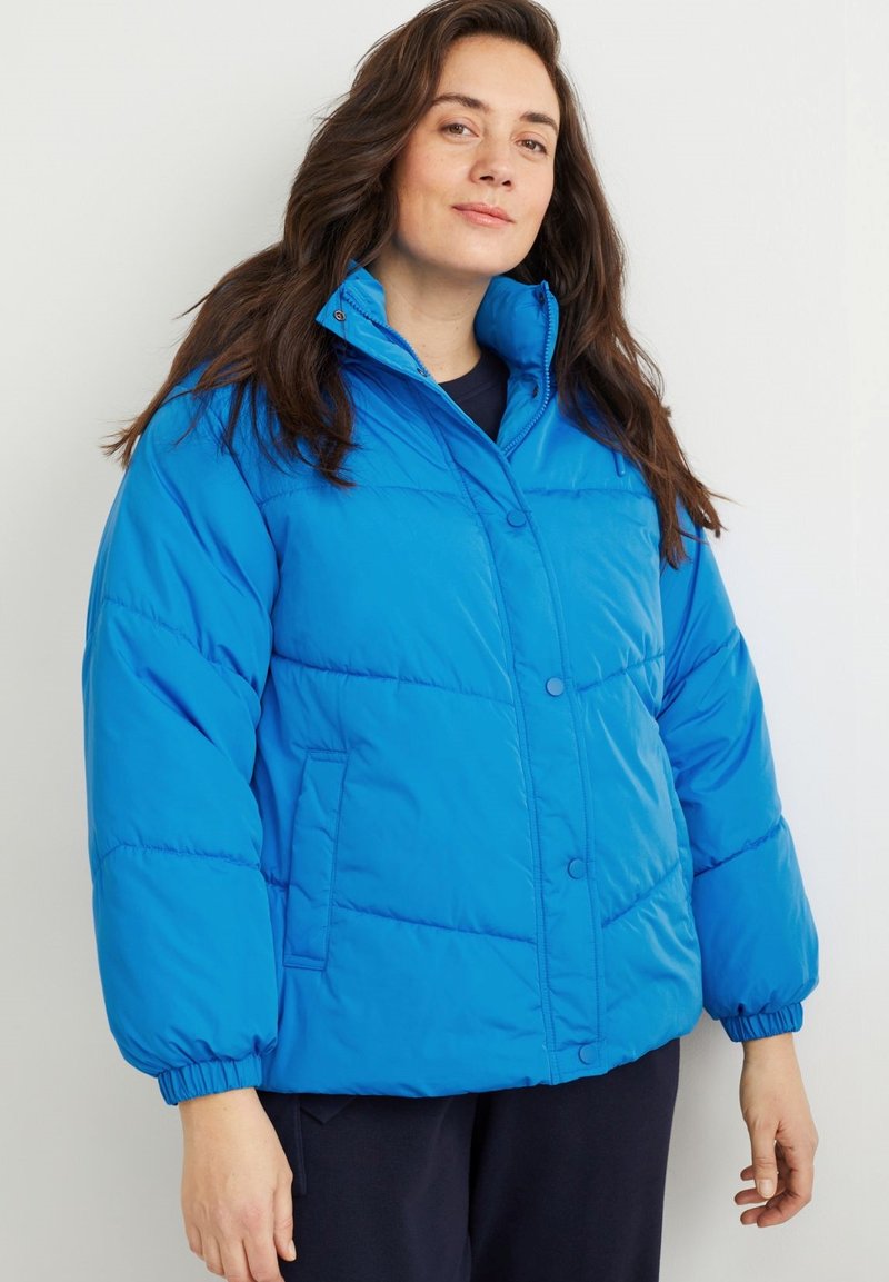 Chaqueta acolchada azul con un alto cuello, cierre de botones al frente y puños elásticos. Presenta paneles cosidos y bolsillos laterales. Tejido suave y ligero.