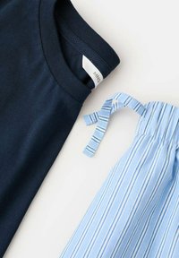 Tummansininen puuvillapaita, jossa on kaulus, yhdessä vaaleansinisen raidallisen hameen kanssa, jossa on sidottu nauhakiinnitys vyötäröllä.