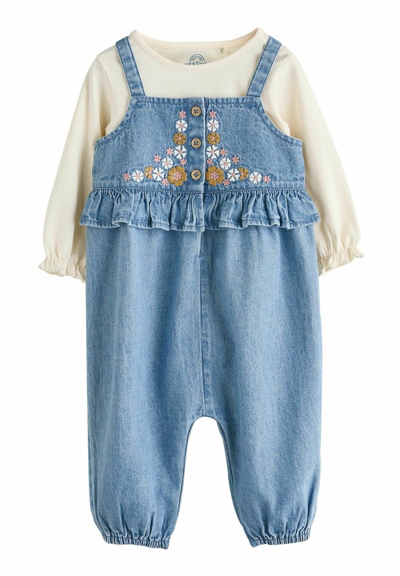 Mono de mezclilla con un dobladillo con volantes, bordado floral en el pecho, botones de madera y una blusa de manga larga beige debajo.