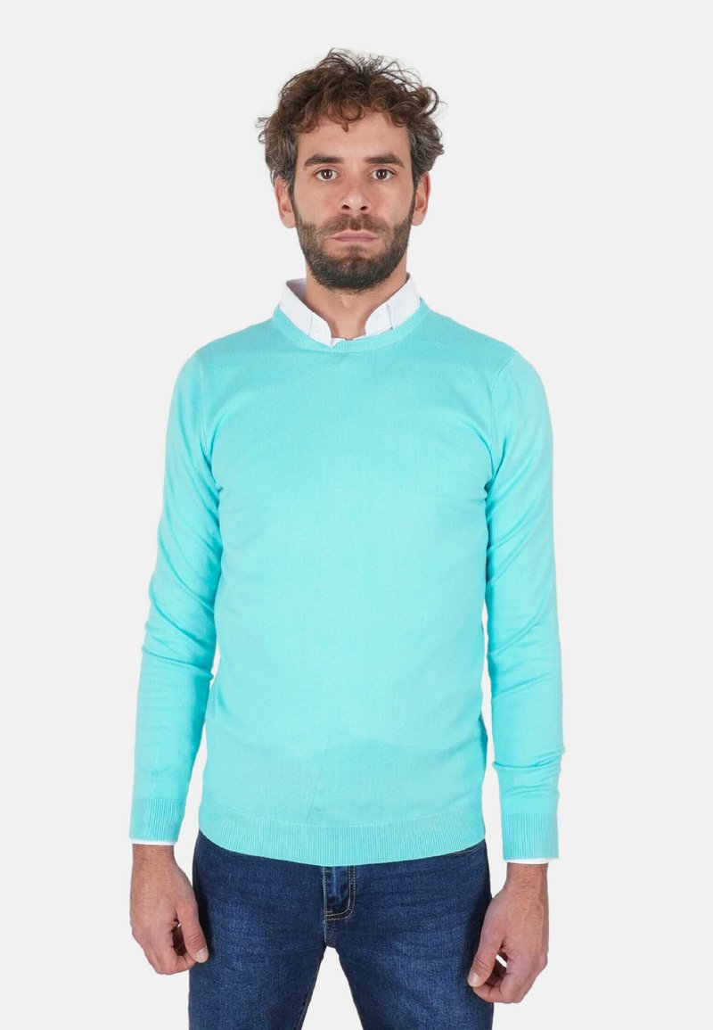 Maglione celeste realizzato in tessuto a maglia liscia, con scollo rotondo e maniche lunghe, indossato sopra una camicia bianca con colletto, abbinato a jeans blu.