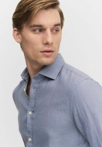 Jasnoniebieska lniana koszula z kołnierzykiem zapinanym na guziki, charakteryzująca się luźnym krojem i subtelną teksturą. Małe guziki zdobiące listwę.