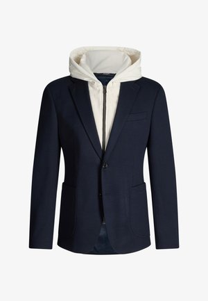 Navy blazer layered over a white zip-up hoodie with a high collar and hood, front pockets, and button closure on the blazer.