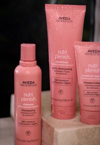 Tre Aveda Nutri Plenish-produkter: schampo i en rosa flaska, balsam och behandlingmask i rosa tuber, alla prydda med vattendroppar.