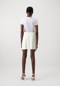 T-shirt bianco a maniche corte, abbinato a una gonna skater gialla pallida, con una trama liscia. Scarpe con tacco alto bianche e con cinturini completano il look.