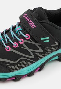 Schwarzer Sportschuh mit pinken und aquafarbenen Akzenten, ausgestattet mit einem strukturierten Obermaterial, auffälliger Markenkennzeichnung und einem sicheren Riemen mit mehrfarbigen Schnürsenkeln.