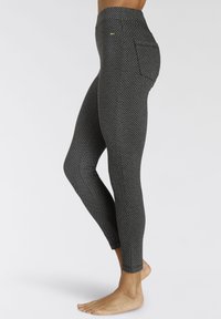 Hoge taille zwarte leggings met geometrisch patroon, gemaakt van rekbaar materiaal, met een zijzak en een gladde textuur.