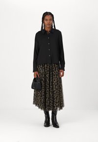 Svart knapp-up skjorta med avslappnad passform, i kombination med en genomskinlig leopardmönstrad kjol. Accessoarer inkluderar en liten svart handväska och knähöga stövlar.