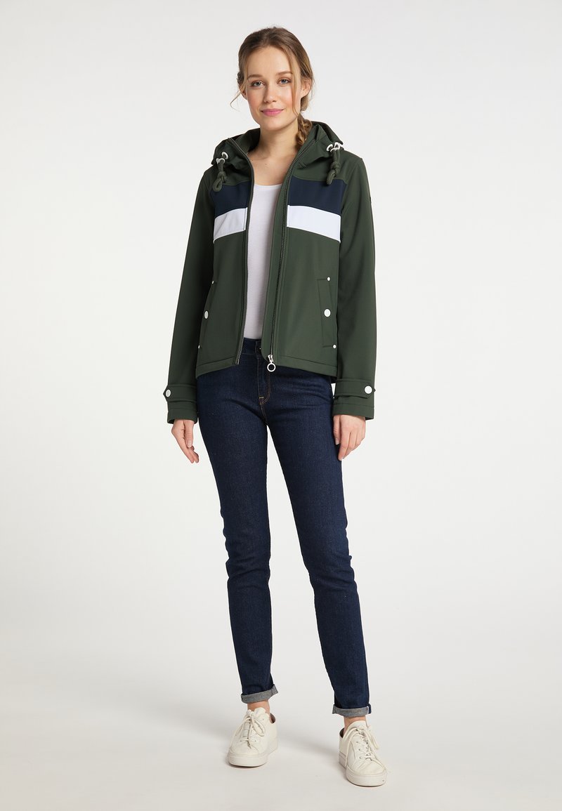 Veste imperméable verte avec des rayures bleu marine et blanches, dotée d'une capuche, d'une fermeture éclair et de poches avant, associée à un jean foncé et des baskets blanches.