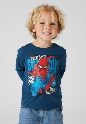Camicia azzurra di cotone a maniche lunghe con una stampa colorata di Spider-Man, con elementi testuali e scollatura rotonda casual. Indossata con dei jeans.