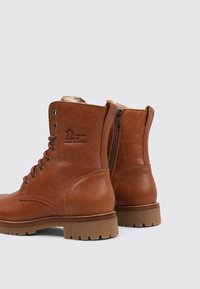 Botas de cuero marrón hasta el tobillo con una superficie suave, cordones en la parte delantera y cremallera lateral. Suela de goma con agarre texturizado, que incluye un detalle de logo.