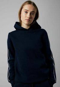 Sudadera azul marino con capucha ajustable, tela texturizada y rayas laterales en blanco que contrastan. Presenta mangas largas y un corte relajado.