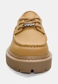 Scarpa in pelle marrone chiaro con punta arrotondata e suola in gomma spessa. Presenta occhielli in metallo, lacci piatti e un accento metallico con marchio sulla linguetta.
