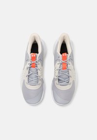 Lys grå atletiske sko med beige accenter og en lys orange flap, der har et mesh-overdel, snørebåndsdesign og polstret sål.
