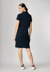 Abito polo navy con maniche corte, colletto e taglio dritto. Abbinato a sneakers bianche con dettagli rossi sul tallone.