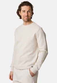 Light beige crewneck sweatshirt made from soft fabric, featuring long sleeves, ribbed cuffs, and a small brand label at the hem.