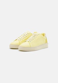 Sneaker gialle in pelle con design a bassa sopra, lacci bianchi, suola in gomma testurizzata e un logo discreto sul lato.