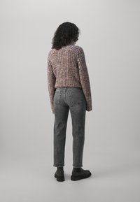 Suéter de punto con un patrón texturizado en varios tonos de púrpura y rosa, combinado con unos jeans gris oscuro y botas negras hasta el tobillo.