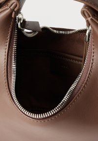 Καφέ δερμάτινη τσάντα χειρός μερικώς ανοιχτή, με ορατό ασημένιο μεταλλικό φερμουάρ και εσωτερική τσέπη από σκουρόχρωμο ύφασμα.