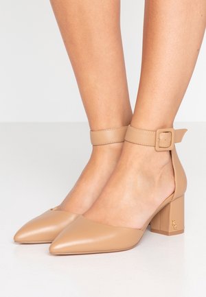 Beige, spitze Pumps mit blockiertem Absatz. Der Knöchelriemen hat eine quadratische Schnalle. Glatte, glänzende Ledertextur mit Logodetail am Absatz.