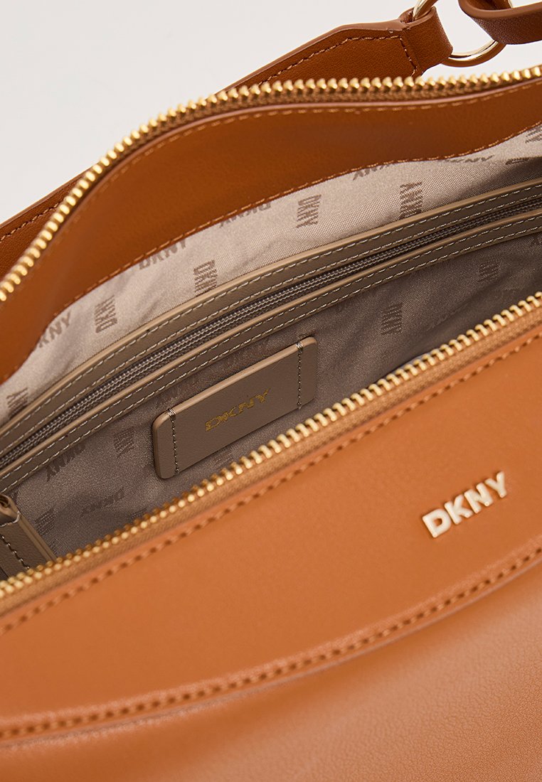 Pomarańczowa skórzana torebka na zamek, charakteryzująca się gładką teksturą, licznymi wewnętrznymi kieszeniami oraz logo DKNY. Wnętrze wyłożone beżową podszewką.