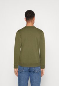 Sudadera verde oliva con cuello redondo, mangas largas y puños de canalé. La tela parece suave y ligeramente texturizada, adecuada para un uso informal.