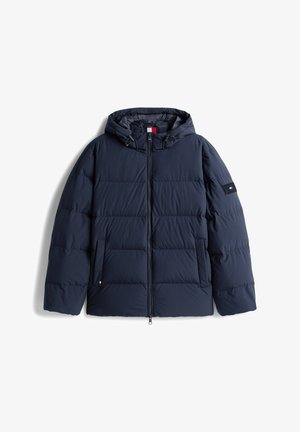 Tamsiai mėlynas apatinis švarkas su gobtuvu, priekiniu užtrauktuku, šoninėmis kišenėmis ir logotipo pleistru kairiajame rankovėje, išdėstytas ant balto fono.