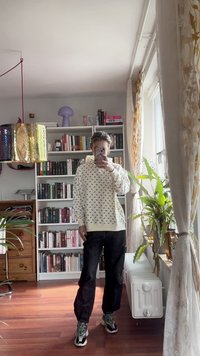 Crème sweatshirt met zwart patroon, capuchon en geribbelde manchetten, gecombineerd met zwarte broek en multicolour sneakers, geplaatst in een heldere kamer.