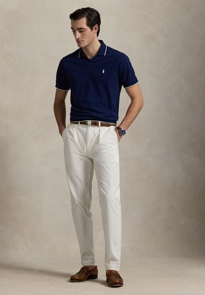 Μπλε ναυτικό πόλο πουκάμισο με λευκή τρέσα, λευκό παντελόνι φόρμας, καφέ δερμάτινα παπούτσια και ρολόι. Απλός σχεδιασμός, εφαρμοστή γραμμή και αντιθετικά χρώματα.