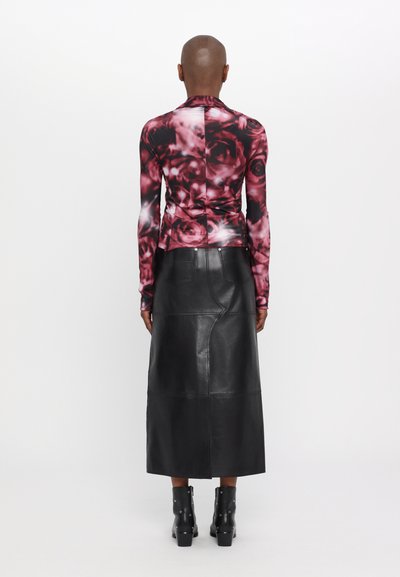 Langärmeliges Oberteil mit einem rot-schwarzen Rosendesign, kombiniert mit einem schwarzen Leder-Midirock mit Nahtdetails und Ankle Boots.