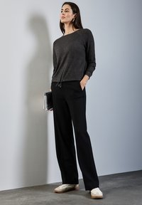 Pantalones negros con cordones combinados con una camiseta de mangas largas gris oscuro. La modelo lleva zapatillas blancas. Los accesorios incluyen un bolso de mano plateado.