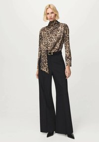 Blusa con stampa leopardata e collo alto, abbinata a pantaloni neri a gamba larga e vita alta con cintura con fibbia dorata. Tessuto liscio e leggero.