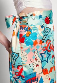 Värikäs kietaisuhame, jossa on eloisa ja leikkisä kuosi, jossa on kuvastoja kuten nopat, tähdet ja käden eleet, valmistettu sileästä ja kiiltävästä kankaasta.