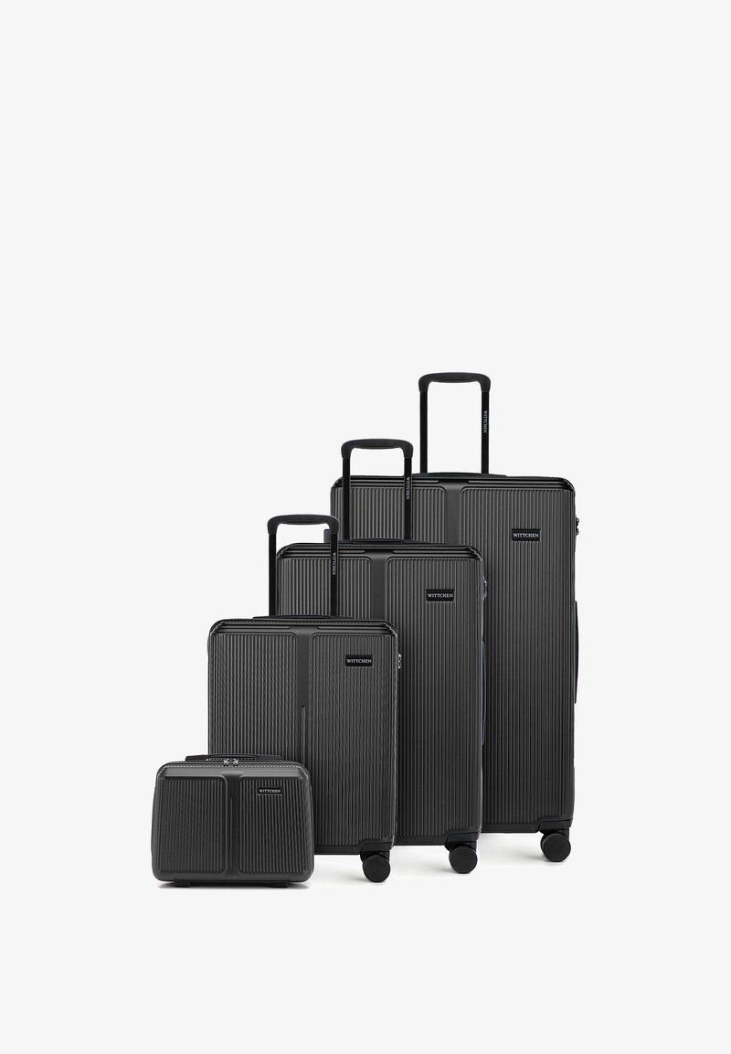 Four black hard-shell suitcases of different sizes with telescopic handles and wheels, arranged from smallest to largest.