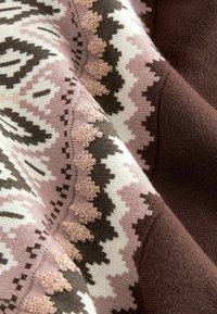 Tissu tricoté avec des motifs géométriques dans des teintes de rose, marron et crème. La texture est douce avec une finition lisse, mettant en valeur des coutures détaillées.