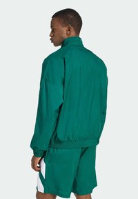 Grön lättviktsjacka med hög krage, elastisk fåll och lös passform, kombinerad med matchande shorts med kontrasterande vita sidopaneler.