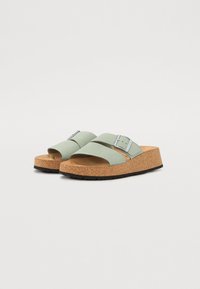 Lichtgroene faux leren sandalen met een kurken wigzool, voorzien van twee banden en een zilveren gespaccent. Getextureerde rubberen buitenzool.