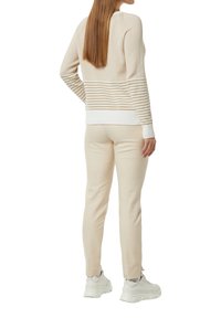 Beige gestreifter Pullover mit gerippten Bündchen und Saum, kombiniert mit cremefarbener Hose und hellgrauen Sneakers. Weiche Textur, lockerer Schnitt.